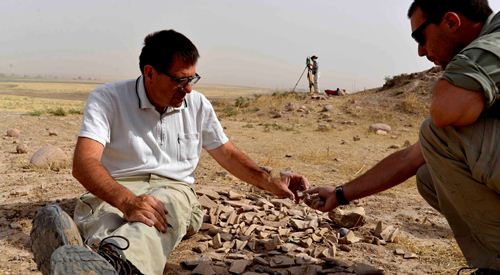 Selekcja ceramiki, Rafał Koliński i Mikołaj Kostyrko, fot. Xenia Kolińska Rafał Koliński i Mikołaj Kostyrko siedzą nad ułożonymi na ziemi fragmentami ceramicznych przedmiotów i selekcjonują je.