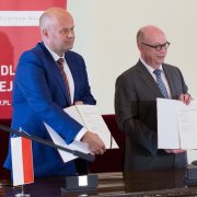 Podpisanie porozumienia między NCN i MPG. Zbigniew Błocki i Martin Stratmann prezentują zebranym gościom podpisaną przed chwilą umowę, trzymając przed sobą otwarte teczki z egzemplarzami dokumentu. Autor zdjęcia: Michał Niewdana.