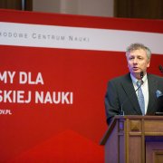 Podsekretarz stanu w MNiSW dr hab. Sebastian Skuza przemawia podczas spotkania otwierającego Dni NCN. W tle znajduje się czerwony baner z napisem Gramy dla polskiej nauki