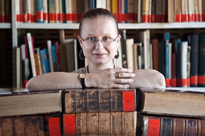 Zdjęcie portretowe Zofii Brozowskiej opierającej się przedramionami o stare księgi