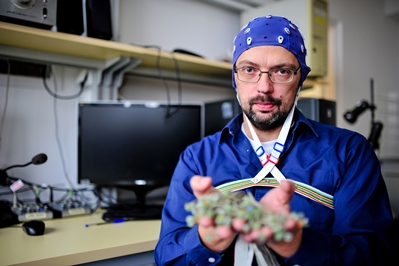 Marek Binder w czepku do EEG, trzymający w rękach elektrody