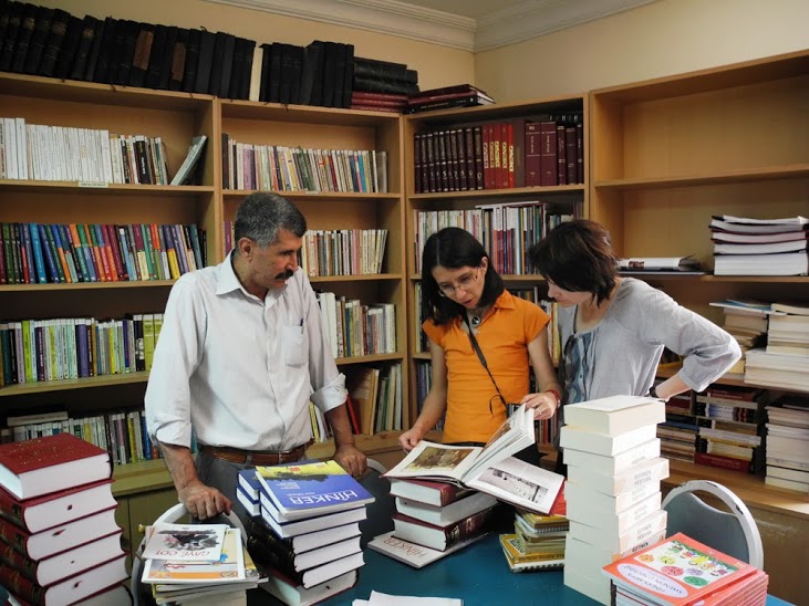 Mężczyzna i dwie kobiety stoją przy stole, na którym leżą książki. Sala znajduje się w Instytucie Kurdyjskim w Stambule