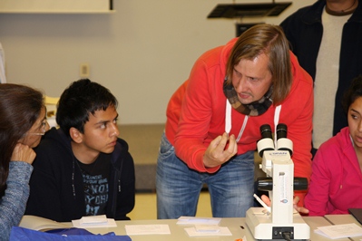 Doktor Adam Flakus rozmawia z grupą dzieci, pochylając się nad mikroskopem