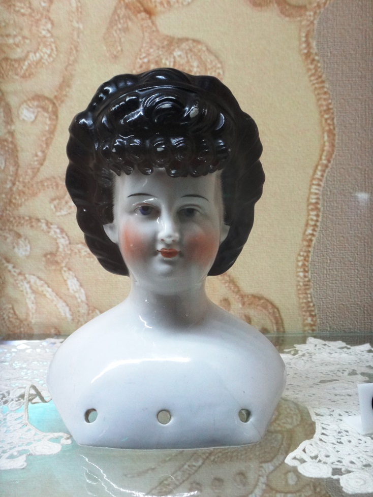 Głowa porcelanowej lalki z czarnymi włosami, znajdującej się w kolekcji Muzeum Zabawy i Zabawek w Kielcach. Fotografia autorstwa Doroty Żołądź-Strzelczyk.