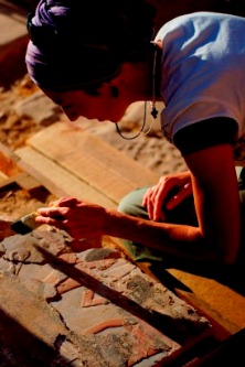 Anastasiia Stupko-Lubczyńska z pędzlem w dłoni pochyla się nad kamiennym blokiem ozdobionym kolorowym reliefem