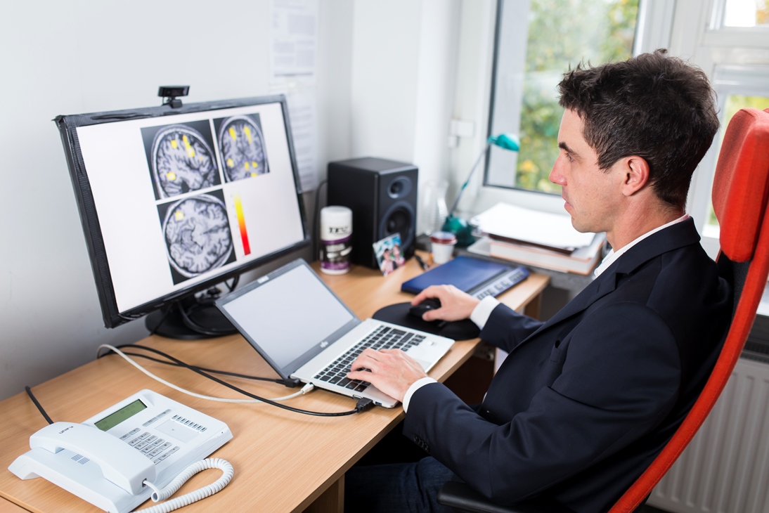 Marcin Szwed siedzi w biurze przed komputerem. Na ekranie komputera wyświetlone są przekrojowe zdjęcia ludzkich mózgów.