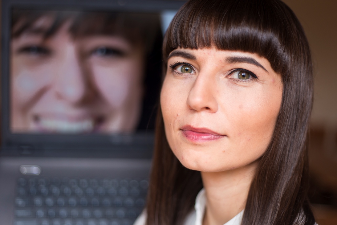 Zdjęcie portretowe Moniki Wróbel. W tle na ekranie komputera widać zdjęcie innej uśmiechniętej kobiety.
