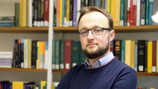 dr Mateusz Grochowski na tle regału z książkami